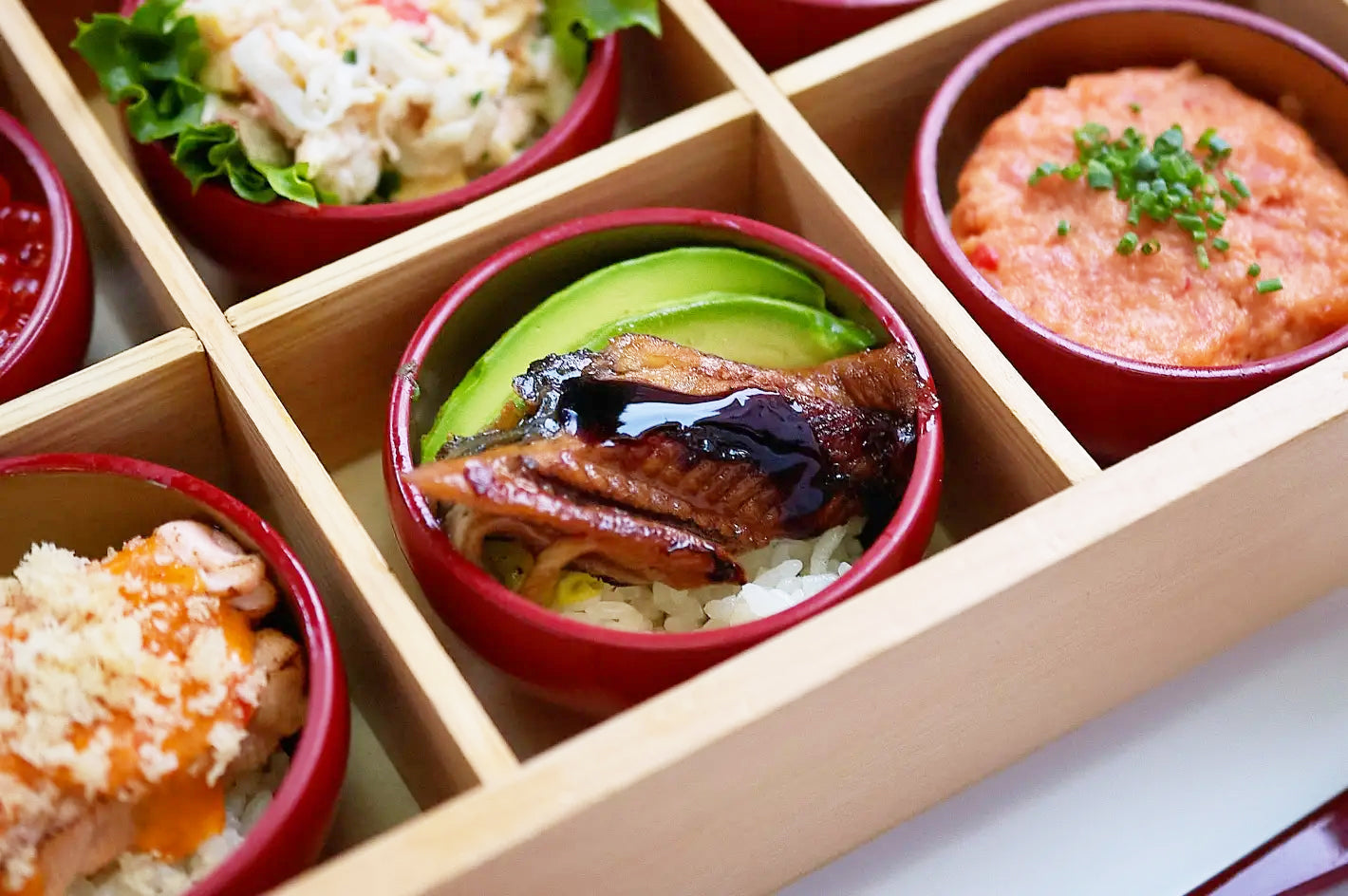Wooden bento box with compartments containing various Japanese dishes.