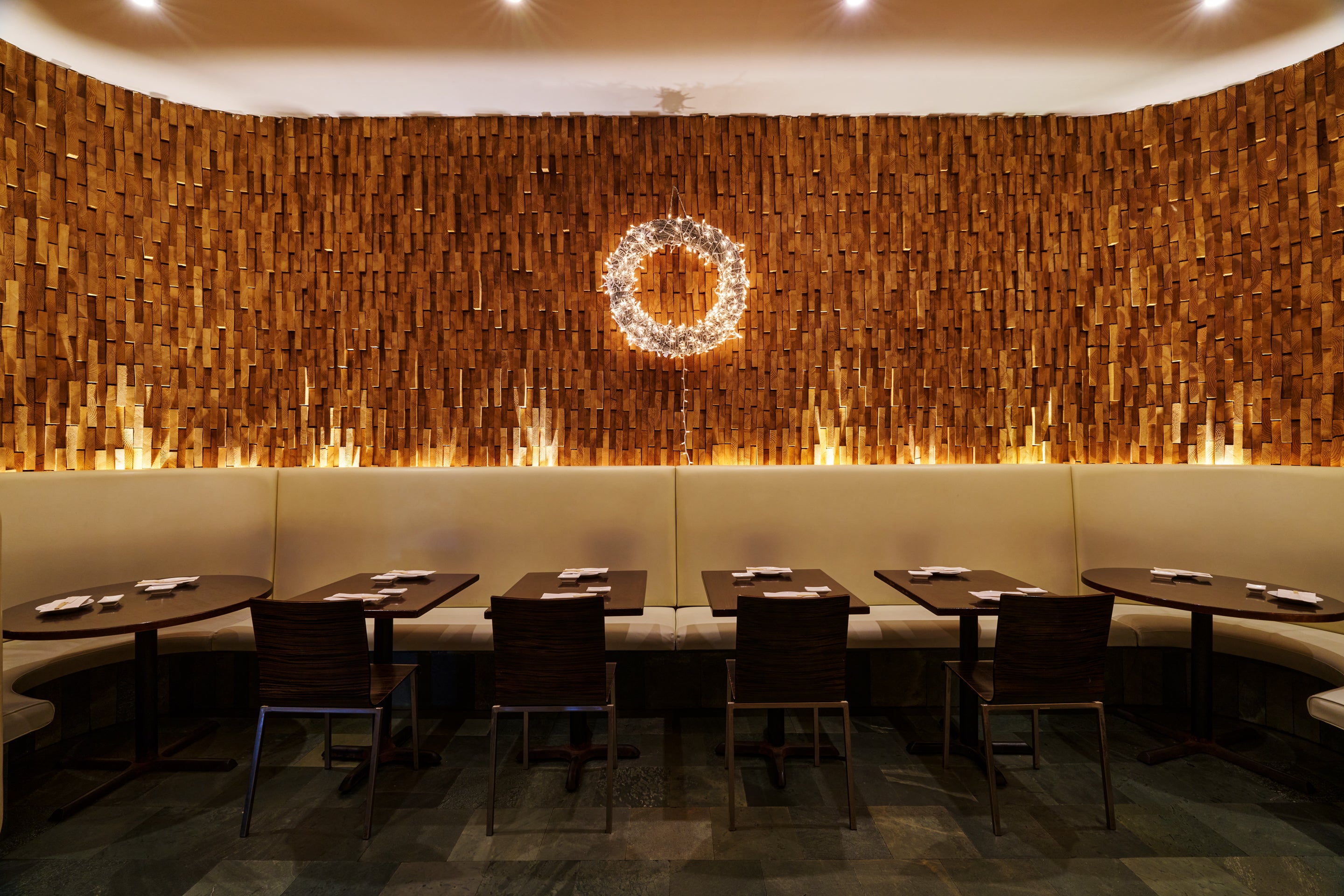 Modern restaurant interior with wooden wall paneling and round tables.