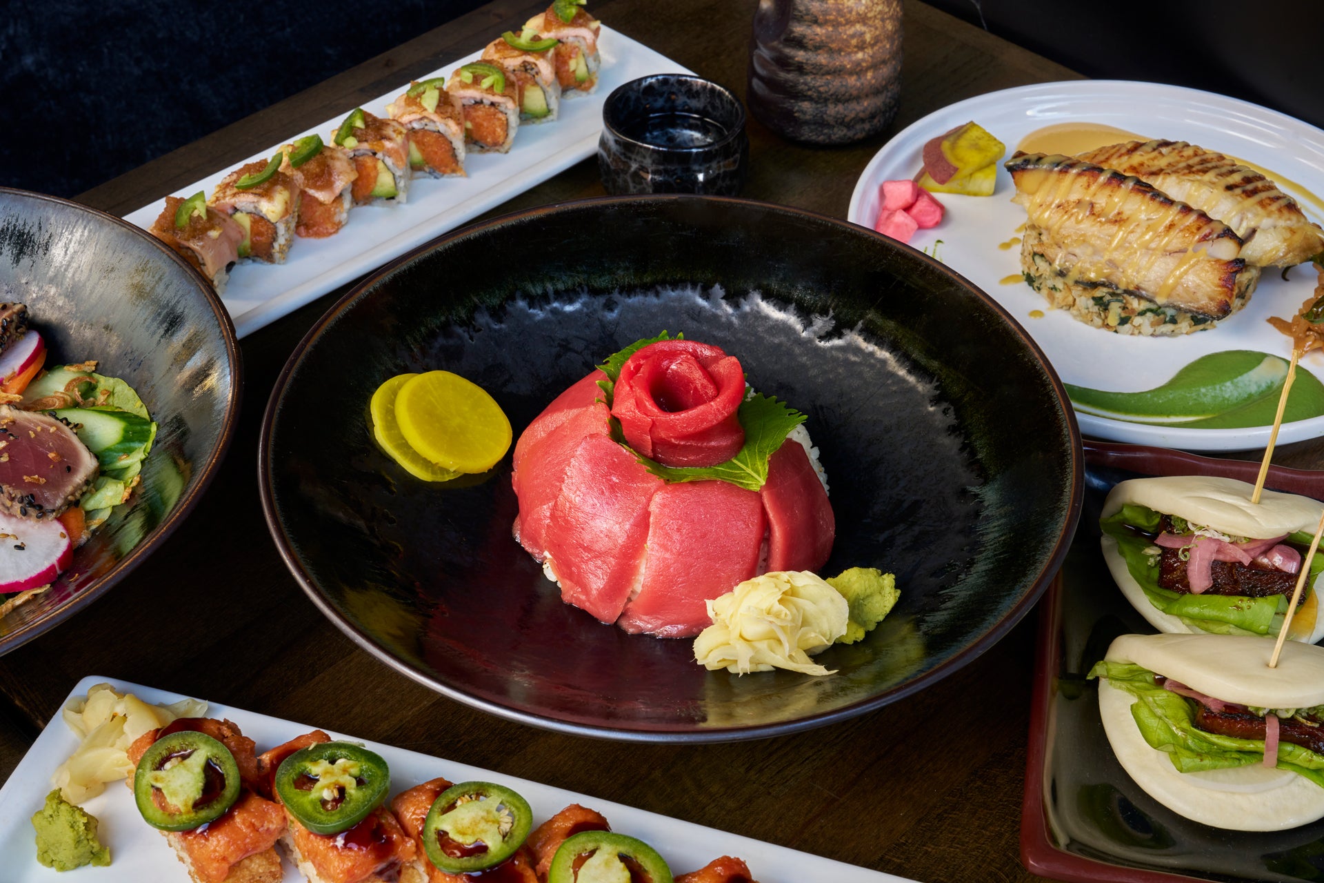 Assorted Japanese cuisine including sushi, sashimi, and a flower-shaped dish on a dark surface.