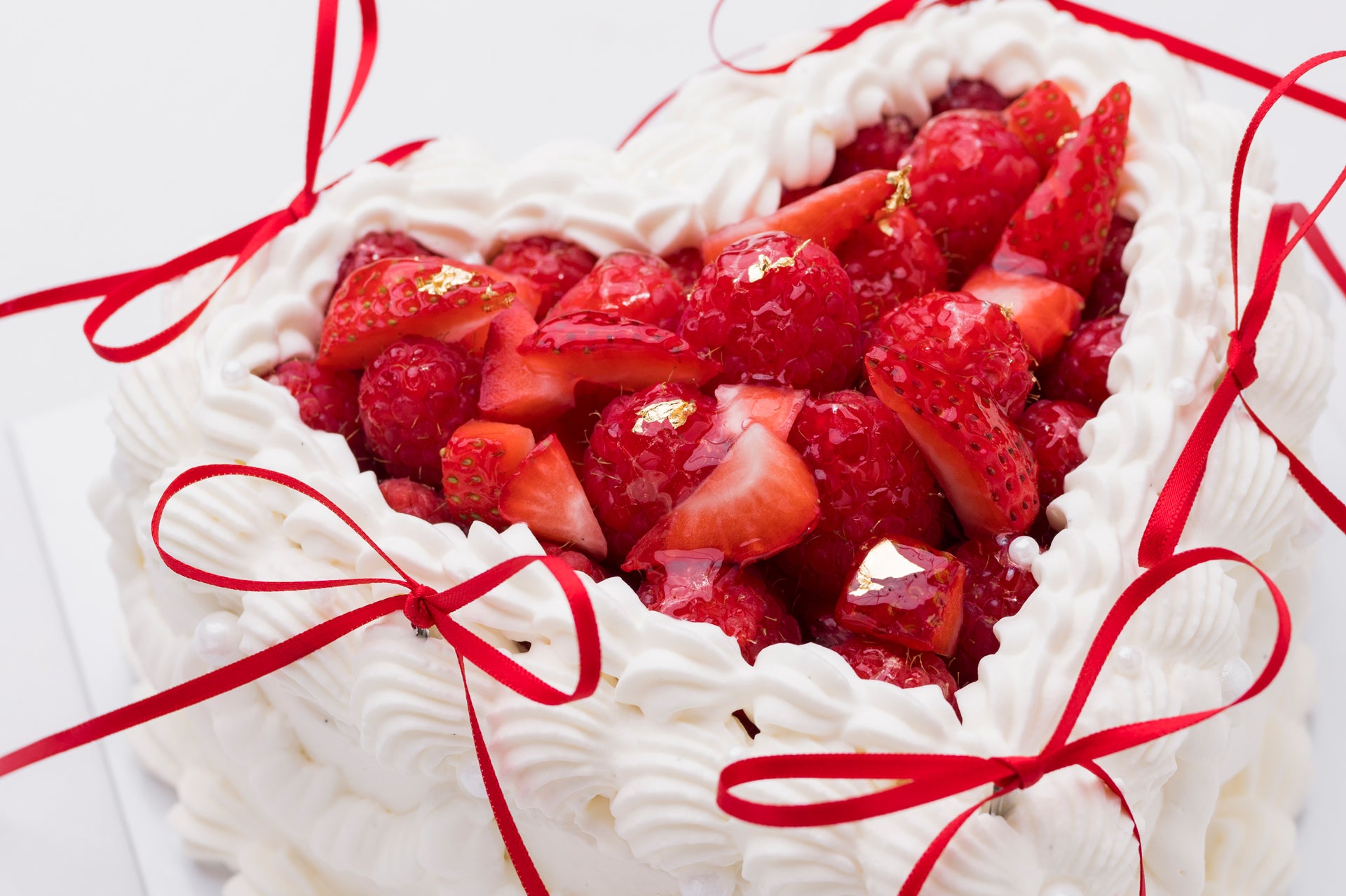 Heart-shaped cake with strawberries and red ribbons.
