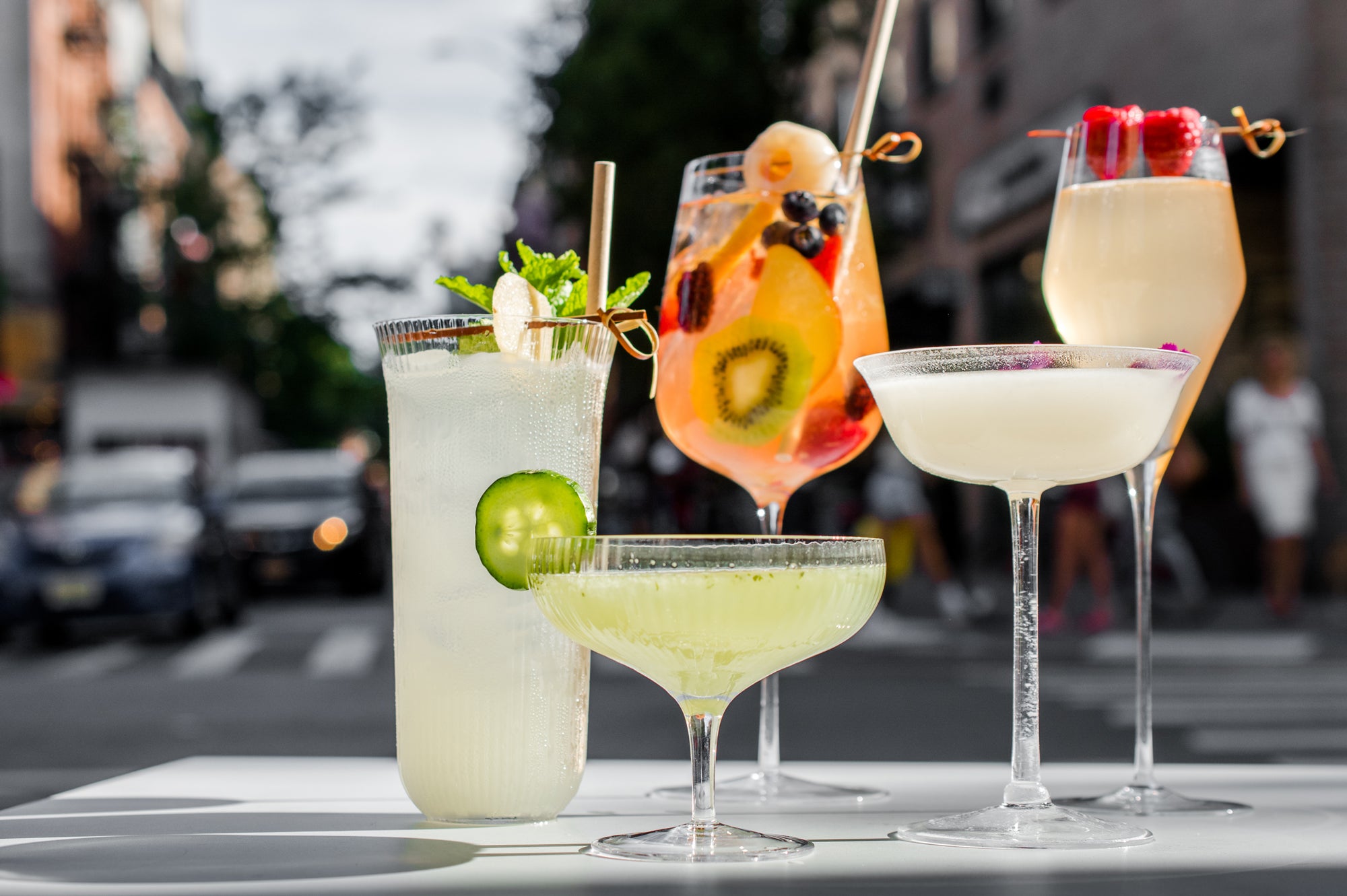 Five colorful cocktails on a table with a blurred street background