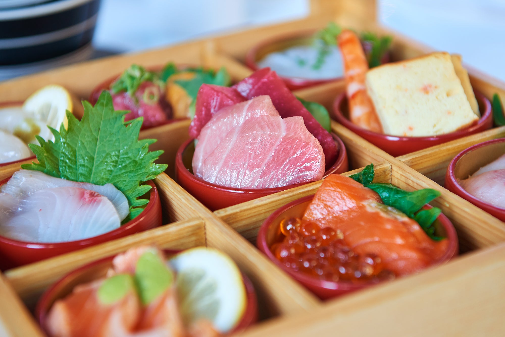 Assorted sushi and sashimi in a wooden box with a blurred background